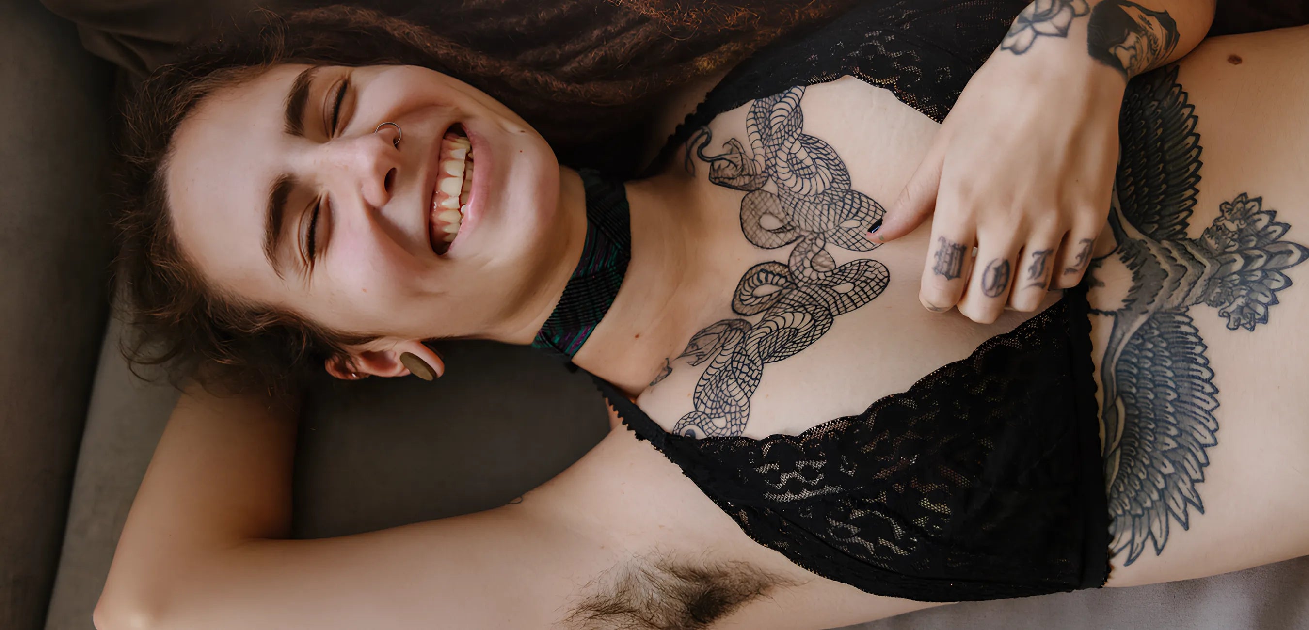 Smiling tattooed person relaxing in black lace lingerie, Bold Humans